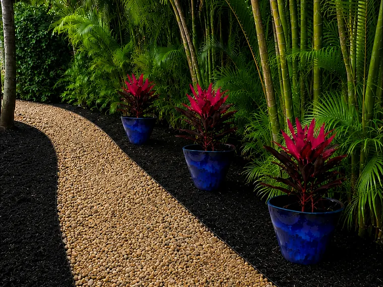 Pebble path through black mulch beds with blue planters, bromeliads and palms